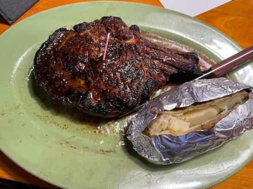 A juicy grilled steak on a green plate, accompanied by a baked potato wrapped in foil.