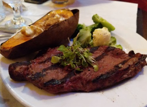 A grilled steak served with a baked sweet potato, broccoli, and cauliflower on a white plate.