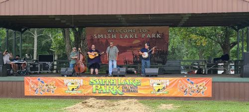 A band performs on stage at Smith Lake Park, with instruments and a welcoming banner in the background.
