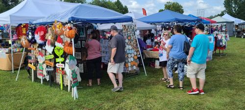 A bustling outdoor market with colorful tents, vendors, and shoppers browsing handmade crafts and decorations.