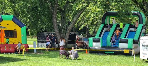 Children and adults enjoy inflatable bounce houses and slides at a park on a sunny day.