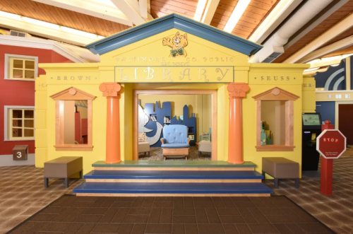 Colorful children's library entrance with whimsical design, featuring bright yellow walls and playful architectural elements.