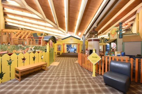 Colorful indoor play area with wooden structures, a yellow fence, and various themed sections for children.