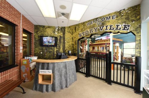 A welcoming children's area named "Storyville" with a nature-themed mural and a reception desk.