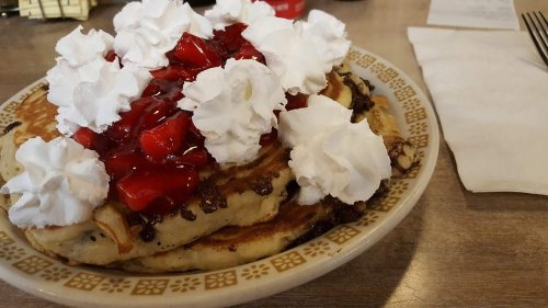 A plate of pancakes topped with whipped cream and strawberry sauce, served in a cozy diner setting.