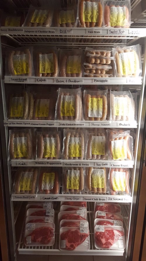 A display case filled with various packaged sausages and meats, labeled with flavors and types.