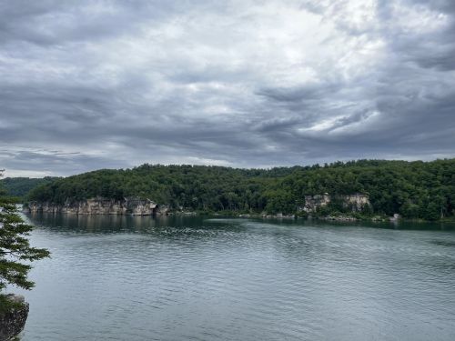 A serene lake surrounded by lush green hills under a cloudy sky.
