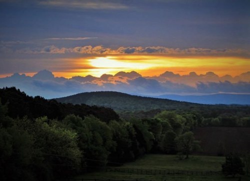 A vibrant sunset over rolling hills, with clouds illuminated in shades of orange and yellow against a twilight sky.