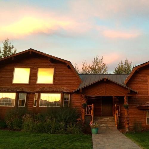 A wooden house with large windows, surrounded by greenery, under a colorful sunset sky.