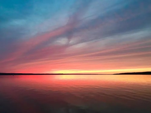 A serene lake at sunset, reflecting vibrant pink and purple hues in the sky and water.