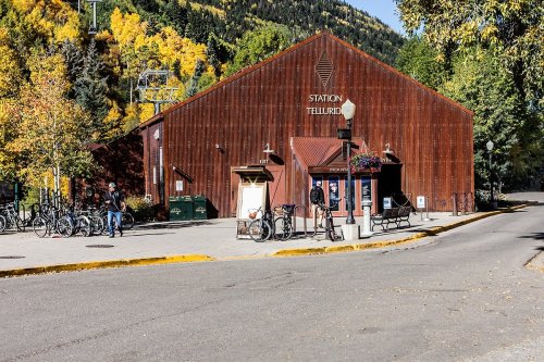A rustic building with a metal facade, surrounded by trees and bicycles, in a scenic mountain setting.