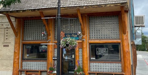 A rustic building with a wooden facade, featuring large glass block windows and hanging flower baskets.