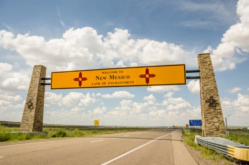 Welcome sign for New Mexico, featuring "Land of Enchantment" against a blue sky with clouds.