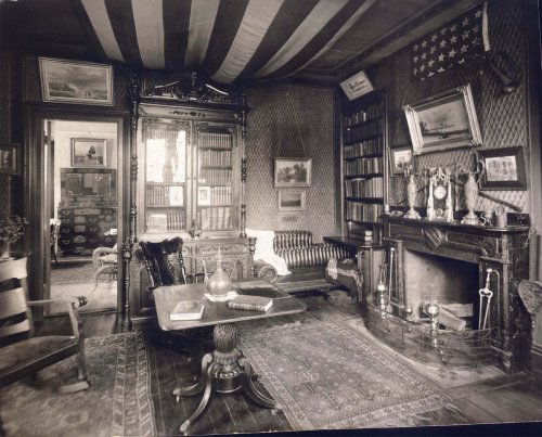 A vintage living room with striped ceiling, bookshelves, a fireplace, and antique furniture, creating a cozy atmosphere.