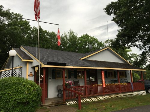 A charming house with a porch, flags flying, surrounded by greenery and flowers.