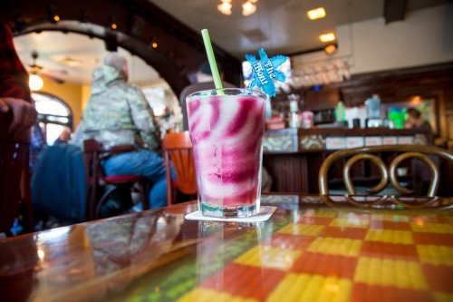 A colorful swirled drink with a straw sits on a table in a lively bar setting.