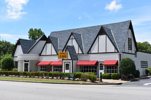 A charming café with a distinctive A-frame design, featuring red awnings and landscaped greenery in front.