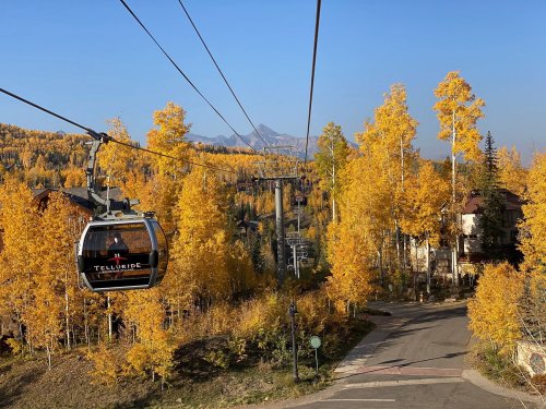 A scenic view of a gondola lift surrounded by vibrant autumn trees and mountains in the background.