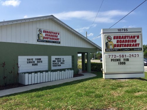 Exterior of Sebastian's Roadside Restaurant, featuring a sign with menu items and contact information. Green grass in front.