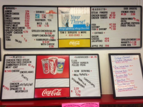 Menu board featuring various food and drink options with prices, including steaks, sandwiches, and sides.