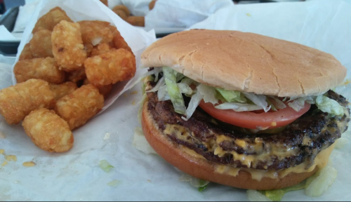 A cheeseburger with lettuce and tomato next to a serving of crispy tater tots on a tray.