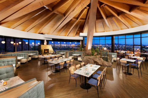 Modern restaurant interior with a high wooden ceiling, large windows, and cozy seating arrangements.