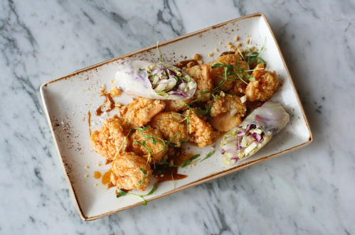 A plate of crispy fried chicken pieces with fresh spring rolls and garnished with herbs on a marble surface.