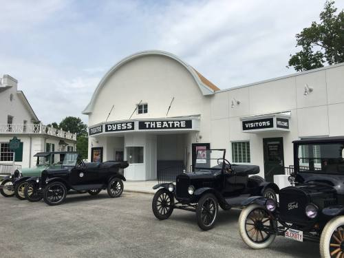 Historic Dyess Theatre with vintage cars parked outside, featuring a white building and a welcoming entrance.