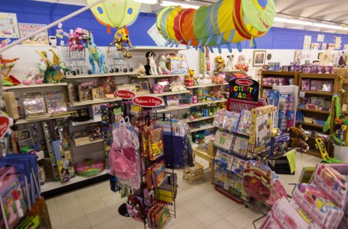 A colorful toy store aisle filled with plush toys, games, and arts and crafts supplies.