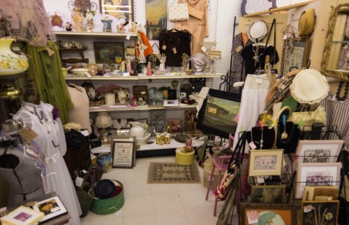 A cluttered vintage shop filled with various antiques, clothing, and decorative items on display.