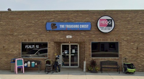Exterior of a brick building featuring "The Treasure Chest" sign and a circular sign for "HEGG" with strollers outside.