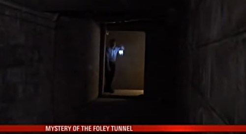 A person holding a flashlight stands in a dimly lit tunnel, exploring the mysterious Foley Tunnel.