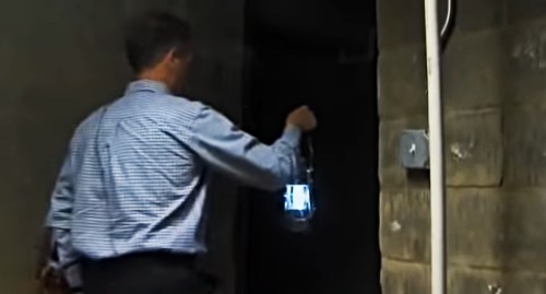 A person in a checkered shirt holds a lantern while entering a dark corridor.