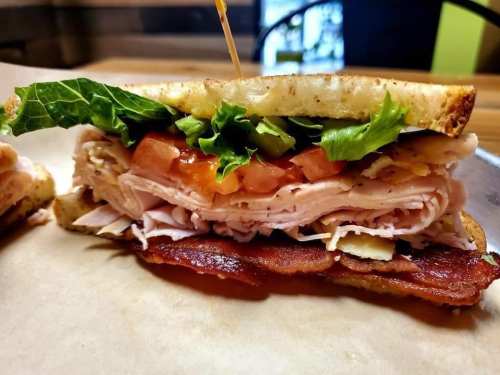 Close-up of a sandwich with layers of turkey, bacon, lettuce, tomato, and pickles on toasted bread.