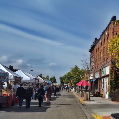 A bustling street market with vendors under tents, people browsing, and a clear blue sky overhead.