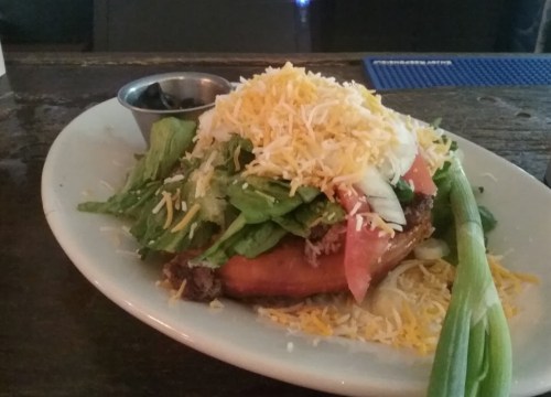 A plate with a large taco topped with lettuce, tomatoes, cheese, and green onions, served with a side of olives.