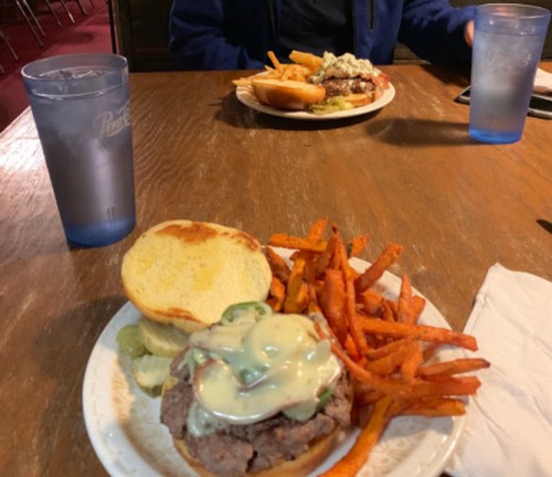 A plate with a burger topped with cheese and jalapeños, served with sweet potato fries, and another plate in the background.
