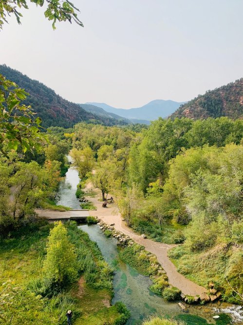 A scenic view of a winding river surrounded by lush greenery and mountains in the background under a clear sky.