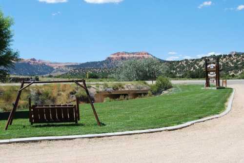 A wooden swing set on green grass near a pond, with red rock formations and blue sky in the background.