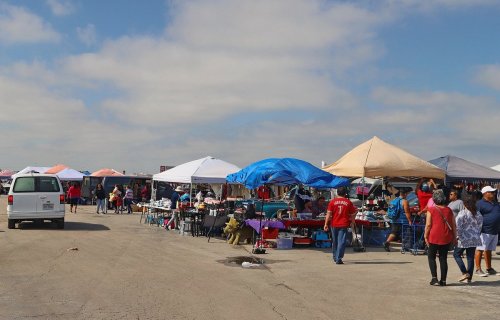 A bustling outdoor market with colorful tents, vendors, and shoppers browsing various goods under a cloudy sky.