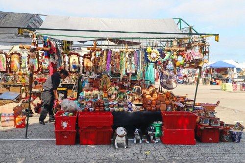 A vibrant market stall filled with colorful crafts, pottery, and decorations, with a vendor arranging items.