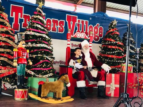 A child sits on Santa's lap in front of decorated Christmas trees and festive gifts at Traders Village.