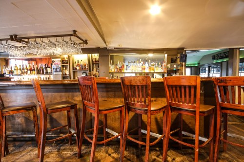 A cozy bar interior featuring wooden stools and a well-stocked bar with bottles and glasses on display.