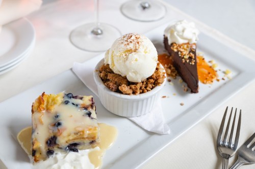 A dessert platter featuring blueberry bread pudding, a crumble topped with ice cream, and a chocolate tart with cream.
