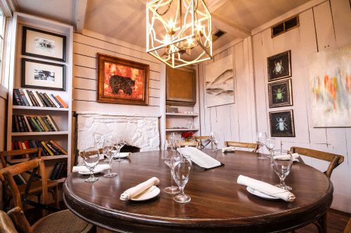 A cozy dining room with a round wooden table set for dinner, featuring artwork on the walls and a modern light fixture.