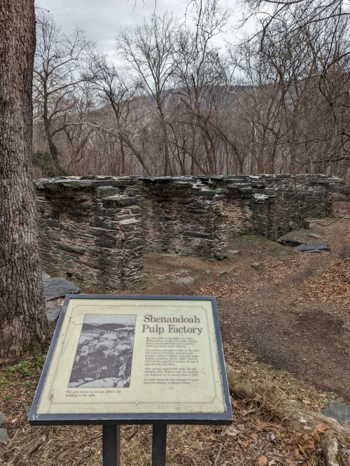Ruins of the Shenandoah Pulp Factory with an informational sign, surrounded by bare trees and rocky terrain.