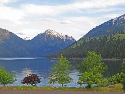 Scenic view of a calm lake surrounded by mountains and lush greenery under a partly cloudy sky.
