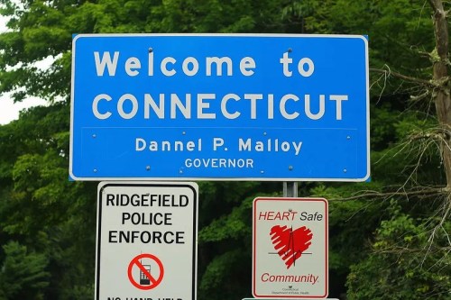 Welcome sign for Connecticut featuring Dannel P. Malloy as governor, with additional signs for police enforcement and community safety.