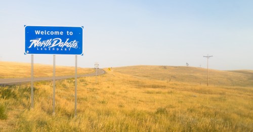 Blue "Welcome to North Dakota Legendary" road sign on Highway 12 surrounded by golden prairie grass.