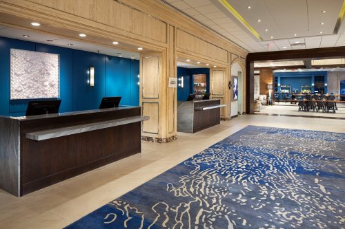 Modern hotel lobby featuring a blue accent wall, two reception desks, and a decorative area rug.